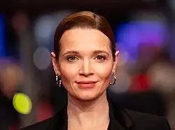 Karoline Herfurth auf der 74. Berlinale 2024 trägt eine schwarze Blazer-Anzug-Kombination mit tiefem Ausschnitt. Gescheitelte kastanienrote Kurzhaarfrisur und silberne runde Ohrringe.