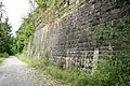 Stützmauer von etwa 1901/02 an der ehemaligen Bregenzerwaldbahn mit aufgesetzten Holzbalken zum Schutz vor Steinschlag (Trasse wird jetzt als Radweg genutzt)