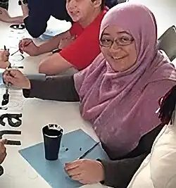 Khairunnisa Ash’ari beim U.S. Embassy Brunei Leadership Program. Eine jugendliche Asiatin mit rosa Kopftuch und Brille beim Schreiben eines Plakates.