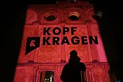 Der Schriftzug Kopf & Kragen Literaturverlag wird mit einem Lichtprojektor auf die Hauptfassade der Ruine des Anhalter Bahnhofs in Berlin geworfen.