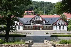 Historisches Fachwerkgebäude mit Schild 'Badehaus' in einer Kuranlage, umgeben von Bäumen und Wald im Hintergrund