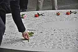 Einweihung des Ländergedenkzeichens, 2025. Eine Rose wird auf eine Scheibe mit eingravierten Ländernamen gelegt.