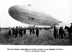 Unscharfes Schwarz-Weiß-Foto eines Luftschiffs in Bodennähe mit Personen und einem Reiter im Vordergrund. An der Hülle des Zeppelins sind ein Balkenkreuz und die Kennung LZ 81 erkennbar.