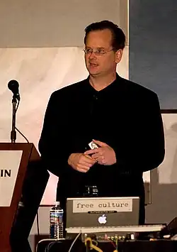 Lawrence Lessig stehend auf einem Podium mit Mikrofon, mit einem Laptop vor ihm.