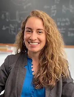 Eine lächelnde Frau vor einem unscharfen Hintergrund.