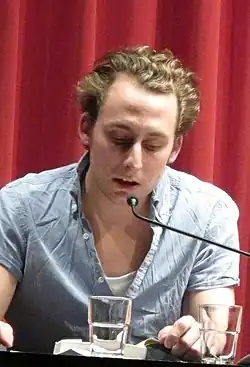 Christopf Szalay spricht in ein Mikrofon, vor ihm ein Wasserglas