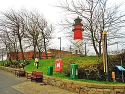 Der gelbe Tassenpegel neben dem grünen Tideschreibpegel unterhalb des Leuchtturms, links der Ankerfriedhof
