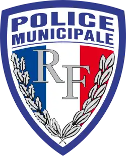 Abzeichen der Police municipale in Form eines Franzosenschildes (das heißt unten spitz zulaufend, oberer Rand leicht konvex gebogen). Der Rand ist blau, innen steht oben auf weißem Grund „Police municipale“ in serifenlosen Versalien. Die Fläche unterhalb des Schriftzugs wird nahezu vollständig von einer blau-weiß-roten Trikolore eingenommen. Auf dieser befinden sich im Zentrum die Buchstaben „RF“ in silbernen Lettern, eingerahmt von Eichenlaub am linken Rand der Trikolore und Lorbeerlaub an ihrem rechten Rand.