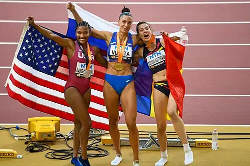 Tara Davis-Woodhall, Ivana Vuleta und Alina Rotaru-Kottmann mit Medaille um den Hals halten hinter ihrem Körper die jeweilige Landesflagge hoch.