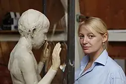 Skulptur eines Jungen mit erhobenen Händen, ihr gegenüber Lotta Blokker, die in die Kamera blickt