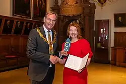 Links im Bild sieht man Burkhard Jung, den Oberbürgermeister der Stadt Leipzig, der zu diesem feierlichen Anlass seine Amtskette trägt. Rechts im Bild sieht man Simone Schwarz, die mit dem Louise-Otto-Peters-Preis 2024 der Stadt Leipzig geehrt wird. Beide stehen im historischen Festsaal des Alten Rathauses Leipzig.