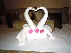 Handtücher zu sich an den Schnäbel berührenden Schwänen geformt, auf einem Bett platziert