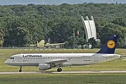Im Vordergrund das Flugzeug auf einer Rollbahn, im Hintergrund das Denkmal