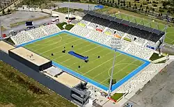 Ein Hockeystadion aus der Vogelperspektive. Um das grüne Spielfeld herum stehen Zuschauertribünen