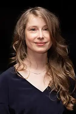 Odine Johne auf dem Empfang des Senders arte anlässlich der Berlinale 2020 in schwarzen langarm Shirt mit V-Ausschnitt. Langes bruentte-blondiertes Haar hängt lockig über der rechten Schulter. Als Schmuck trägt sie eine dezente feingliedrige silberne Kette.