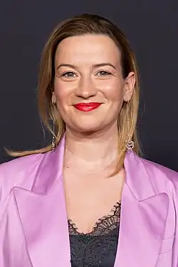 Nina Gummich in einem pinken Blazer vor dunkelgrauem Hintergrund, 2024