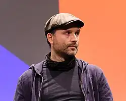 Marc Uwe Kling auf Bühne mit buntem Hintergrund, Halbprofil