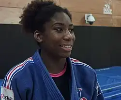 Gahié trägt einen blauen Kampfanzug.