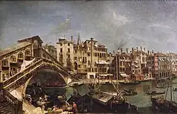 Ölgemälde eines Flussufers mit Handelsbooten und Menschen, die Waren ausladen. Links führt eine überbaute Bogenbrücke zum anderen Ufer, an der eine lange Häuserreihe mit schlichter Fassade und Schornsteinen bis rechts geht.