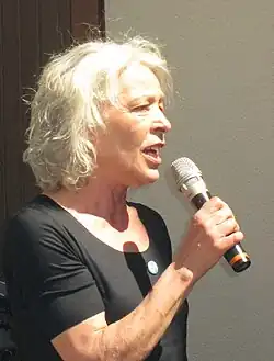 Martina Häusler vor einem Haus, Mikrofon in der Hand