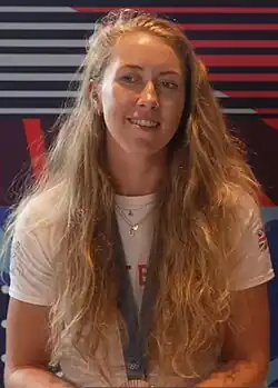 Mathilda Hodgkins-Byrne im weißen T-Shirt der britischen Mannschaft. An einem blauen Band, das sie um den Hals trägt, ist ihre Olympiamedaille erkennbar.