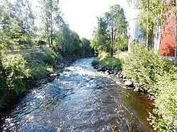 Foto eines Flusses, der durch einen Ort fließt, an der rechten Seite liegen größere Gebäude