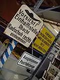 Schild: Vor­sicht! Ein­hemm­stel­le, Obacht, Rad­schuh rechts ein­hem­men!
