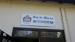 Das Bild zeigt ein weißes Schild auf dem „Van de Merwe Museum“ steht.