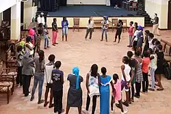 Mary Summer leitet einen Musikworkshop im Senegal, zu sehen sind die Teilnehmerinnen und Mary in einem Kreis, ca. 40 Personen