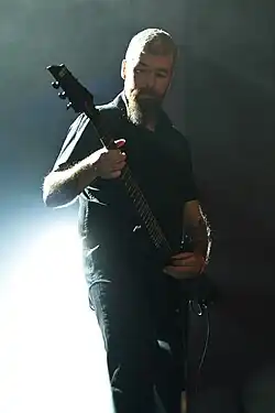 Der von unten fotografierte vollbärtige Calvin Robertshaw spielt mit Beleuchtung im Rücken Gitarre