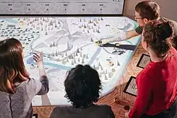 Vier erwachsene Menschen benutzen einen digitalen Spieletisch zum Thema erneuerbare Energien.