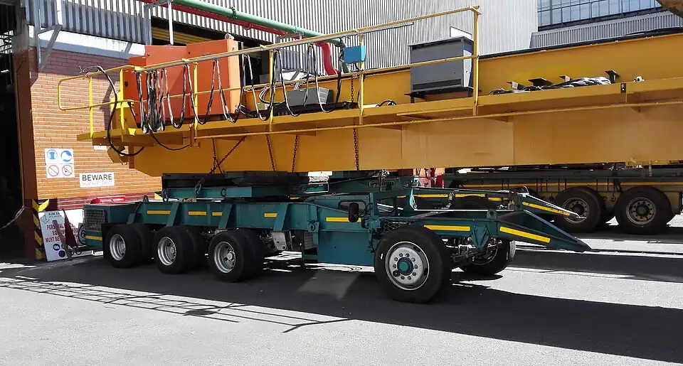 Nachläufer für den Transport von Kranbrücken. Die Lenkung wird durch einen Schwigger bedient, dessen Kabine unter der Ladung hinter der ersten Achse des Nachläufers sitzt.