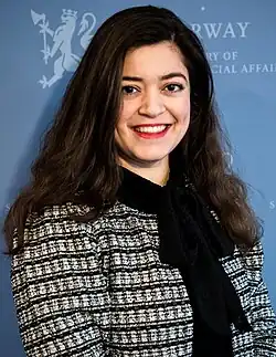 Foto einer Frau, die vor einer blauem Hintergrund mit einem Regierungssymbol steht