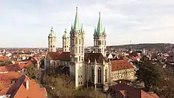 Von einer Drohne aus aufgenommen, Blick schräg auf den Dom mit zwei Türmen mit kupfernen Spitzen vorne und zwei kleineren Türmen mit Kuppel-artigen Spitzen hinten, im Hintergrund die Häuser der Stadt mit roten Ziegeldächern