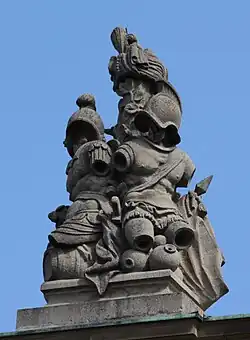 40. Trophäe – Baumstamm, Turban, Harnische mit Helm, Fass, Vasen, Lanzenfahne.