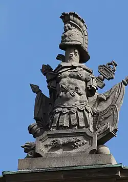 42. Trophäe – Baumstamm, Helm, Schwerter, Harnisch, Liktorenbündel, Mörser, Lanzenfahnen, Kugeln, Relieftafel mit Blitzbündel des Jupiter.