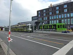 Zentral ist der Mittelhochbahnsteig mit Betondach abgebildet. Die Kamera blickt etwa nach Nordost. Links im Bild ein TW-2500-Paar, rechts ein TW 6000. Die im Vordergrund nach rechts (Südwesten) dem Fotografen entgegenkommende Richtungsfahrbahn der Lister Meile hat drei Richtungsfahrstreifen. Ganz links, die Hochstraße Berliner Allee. Rechts oben die Spielbank Hannover mit glatter brauner Fassade und grün bis blau spiegelnden Fenstern.