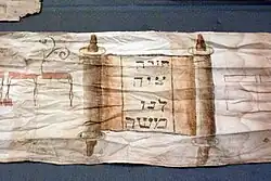 Torawimpel für Nathan bar Chajjim von 1888, mit Abbildung einer Torarolle und der Inschrift: „Eine Weisung hat uns Mosche geboten“ (vgl. Dtn 33,4&nbsp;EU)