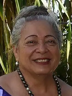 Niki Rattle, die Sprecherin des Parlaments der Cookinseln auf dem mit Schnitzereien verzierten Speaker’s Chair 2017. Eine ältere Polynesierin mit hochgesteckten grauen Haaren und einer Blume über dem Ohr im dunklen Kostüm.