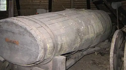 Altes Jauchefass aus Holz mit Gerät zum Befüllen im Hintergrund