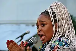 Portraitfoto der Sängerin mit Mikrofon und weißer Rastazopffrisur