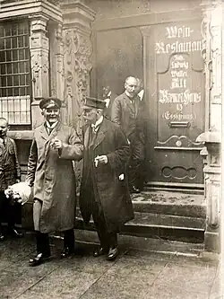 Schwarz-weiß-Fotografie von mehrere Personen, die aus einer Tür ein Gebäude verlassen. An der Tür steht "Wein-Restaurant"