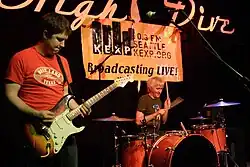 Photo eines Mannes der eine Gitarre spielt und ein Mann der trommelt.