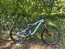 Ein blaues, vollgefedertes Enduro MTB steht vor einer Hecke