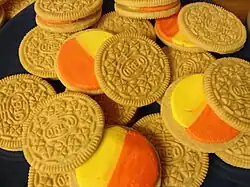 Das Bild zeigt aufgedrehte Oreo-Kekse mit Candy-Corn-Geschmack. Die oberen Hälften sind goldfarben und haben das typische Muster der Marke (mehrere Kreise, die von jeweils vier Dreiecken umgeben sind). Der Oreo-Schriftzug ist mittig in einem Oval platziert. Auf den unteren Kekshälften befinden sich je ein gelber und ein oranger Halbkreis.