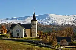 Foto einer weißen Holzkirche, dahinter eine verschneite Berglandschaft
