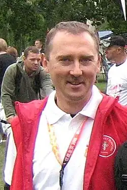 Ostrowski trägt ein weißes Polohemd und darüber eine rote Weste.