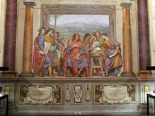 Ölgemälde einer Männergruppe in Togen, die in einem Raum mit Säulen und einer Landschaft im Hintergrund stehen. Der mittlere Mann sitzt und blickt mit den anderen auf eine Büste, die rechts auf einem Hocker steht. Der Raum endet vorne mit einer Kante, die wie eine Wandvertäfelung gemalt ist. Daran sind verzierte Tafeln sowie ein Reliefkopf angebracht.