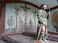 Figur des heiligen Rochus, im Hintergrund Kreuzigungsszene