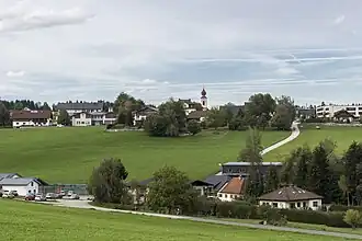Ansicht vom Haushamerfeld-Denkmal. Links unten die Dorfhalle. Schräg rechts darüber das Gemeindeamt mit Feuerwehr. Mittig oben Kirche mit altem Pfarrhof. Rechts oben das Altersheim.